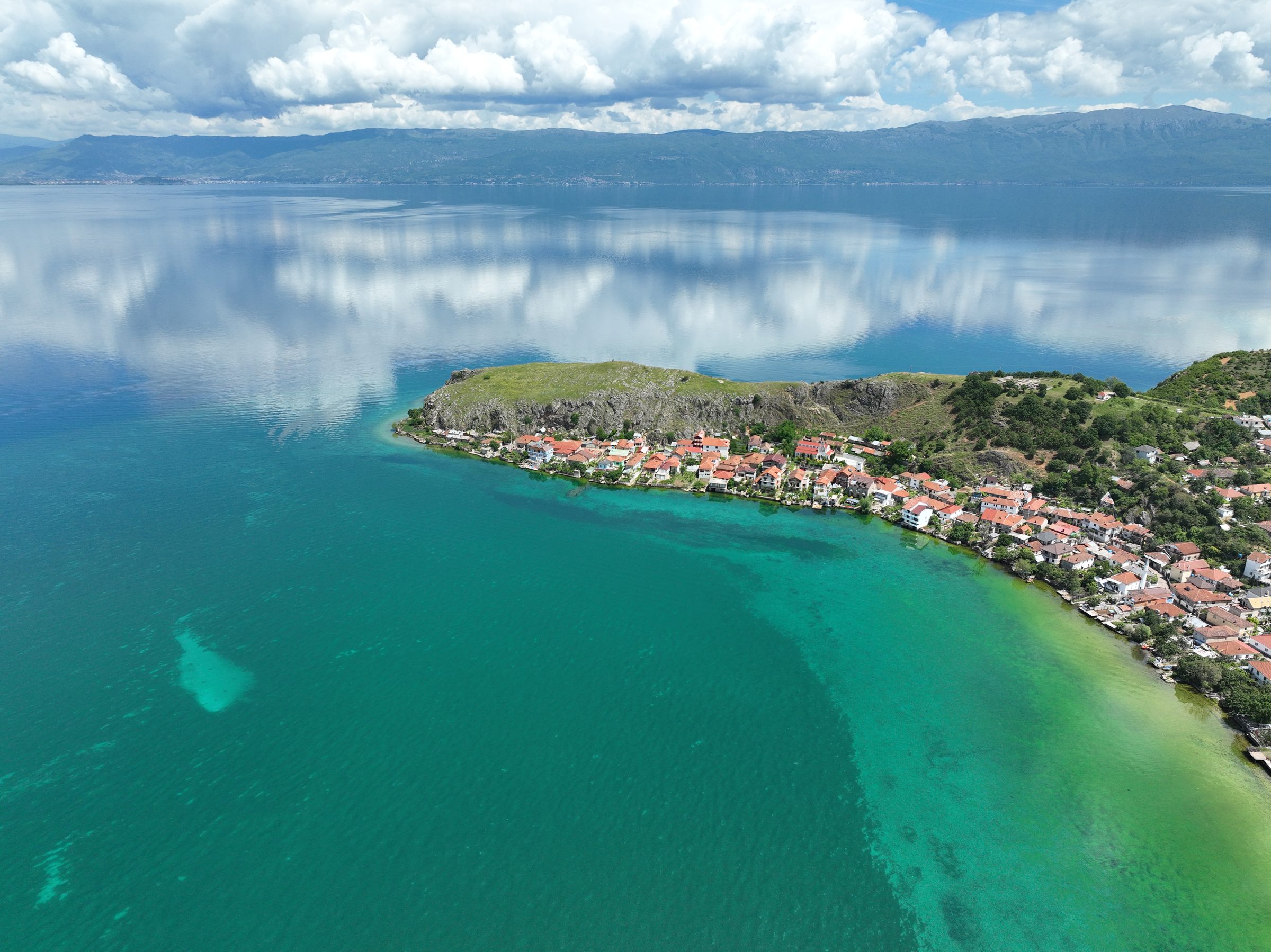 Lin's rocky peninsula reaching into Lake Ohrid, with mirrored clouds on the water