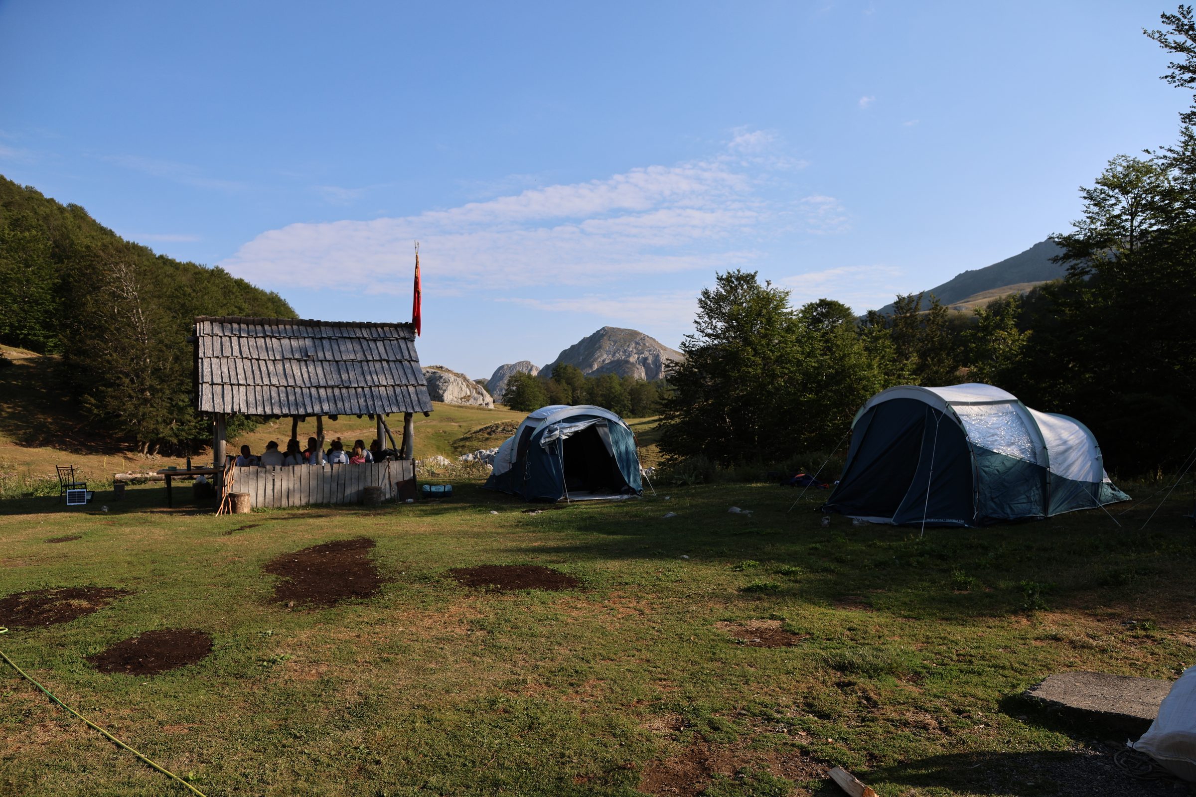 Tents pitched beside a wooden shepherd shelter, mountains behind