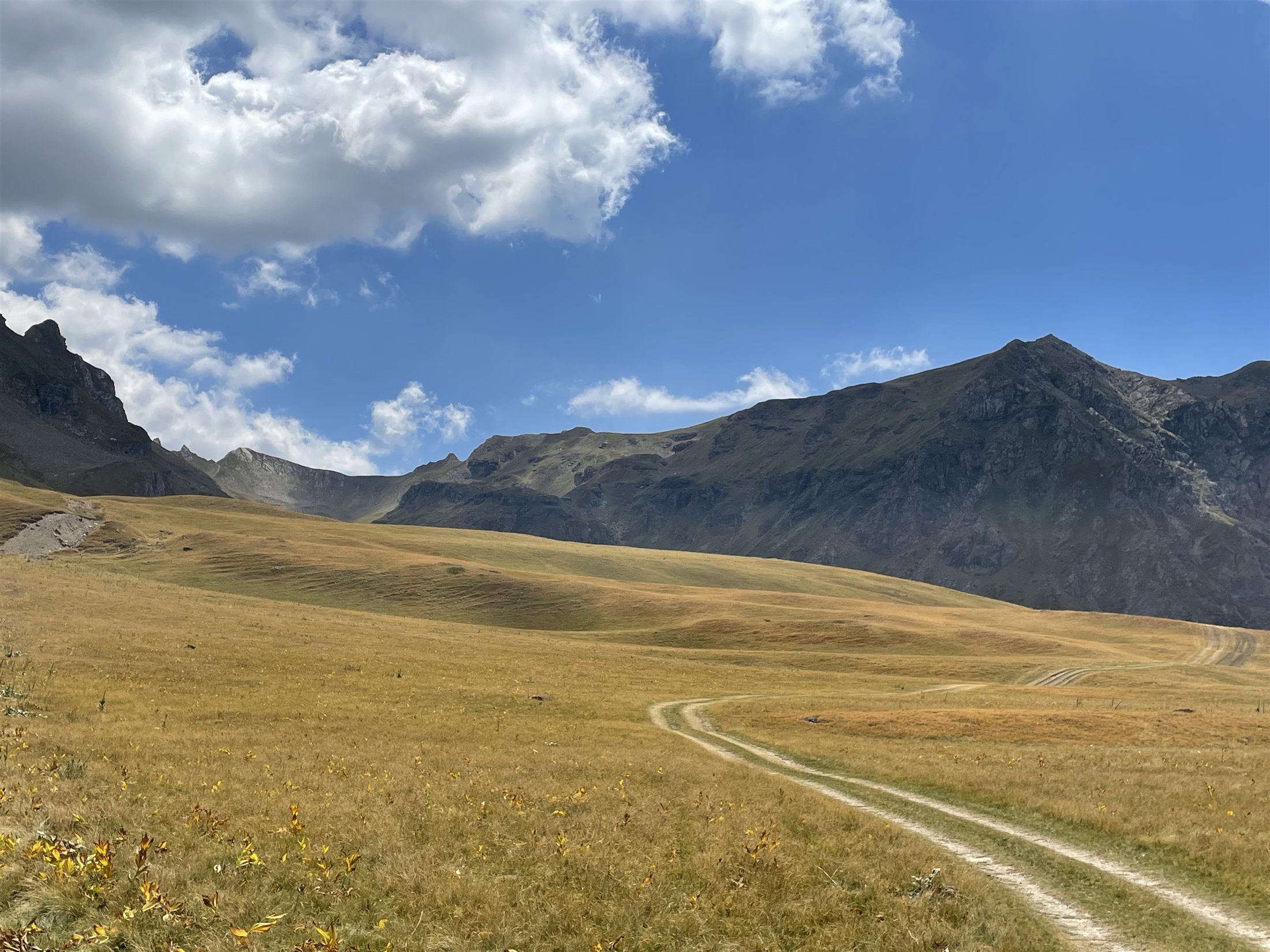 A dirt trail winding through golden highland pasture toward the peaks of Mont Korab