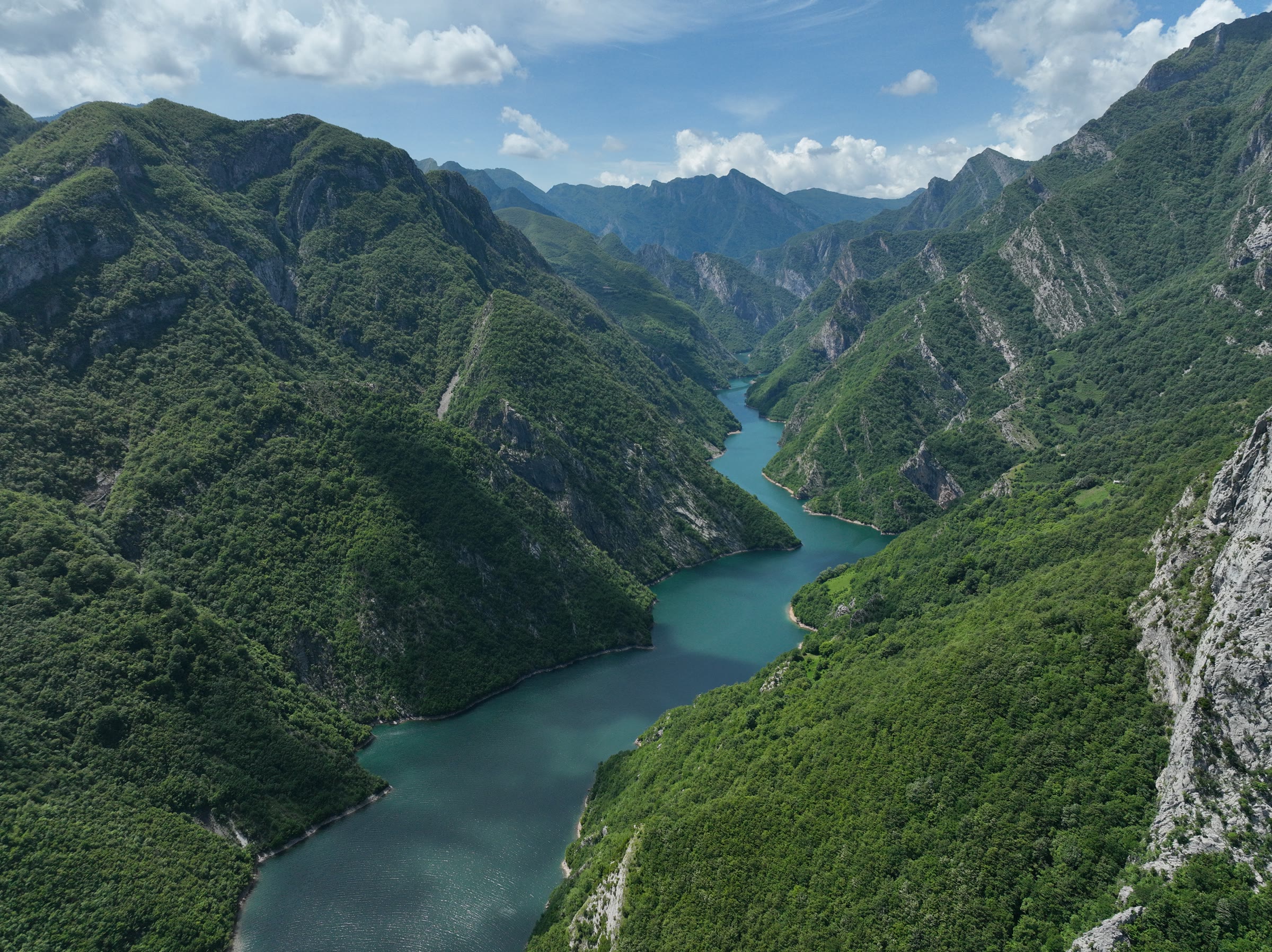 Aerial view of a turquoise river winding through a forested mountain canyon in Albania